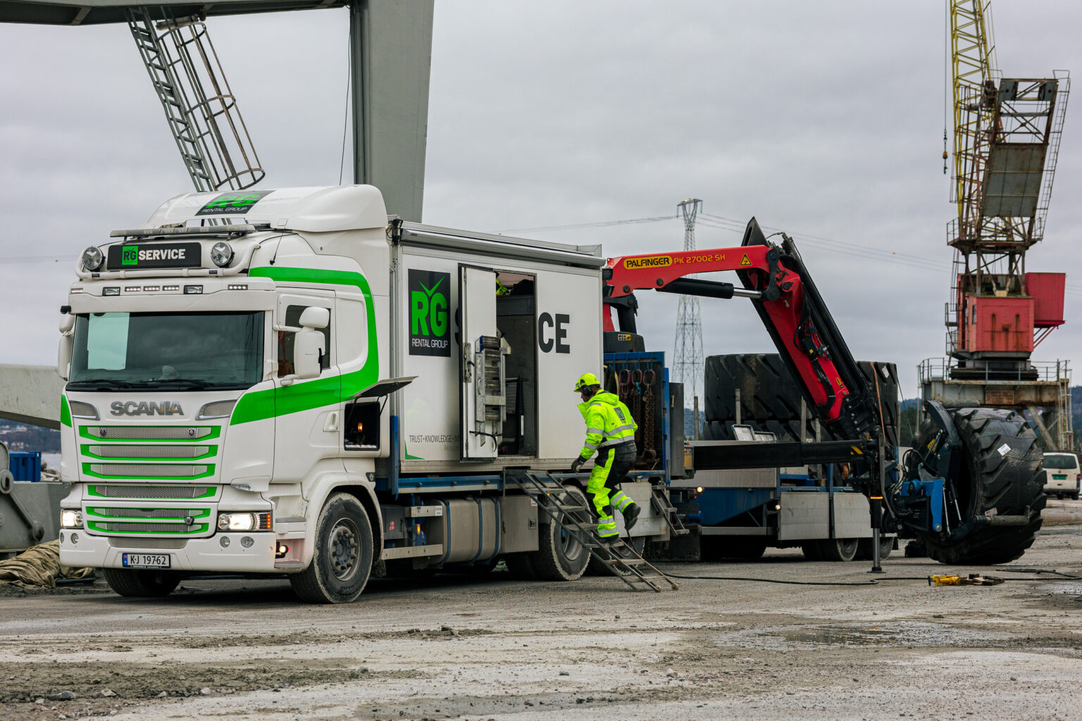 Servicebil fra Rental Group løfter et stort anleggsdekk med kran ute på et industriområde